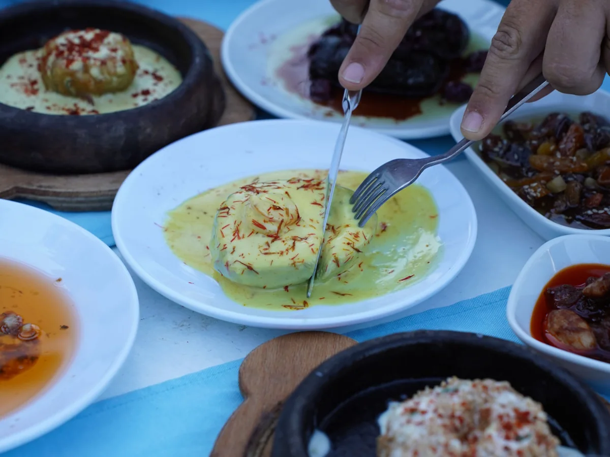 Shared meze dishes on a blue tablecloth, with a guest cutting a portion