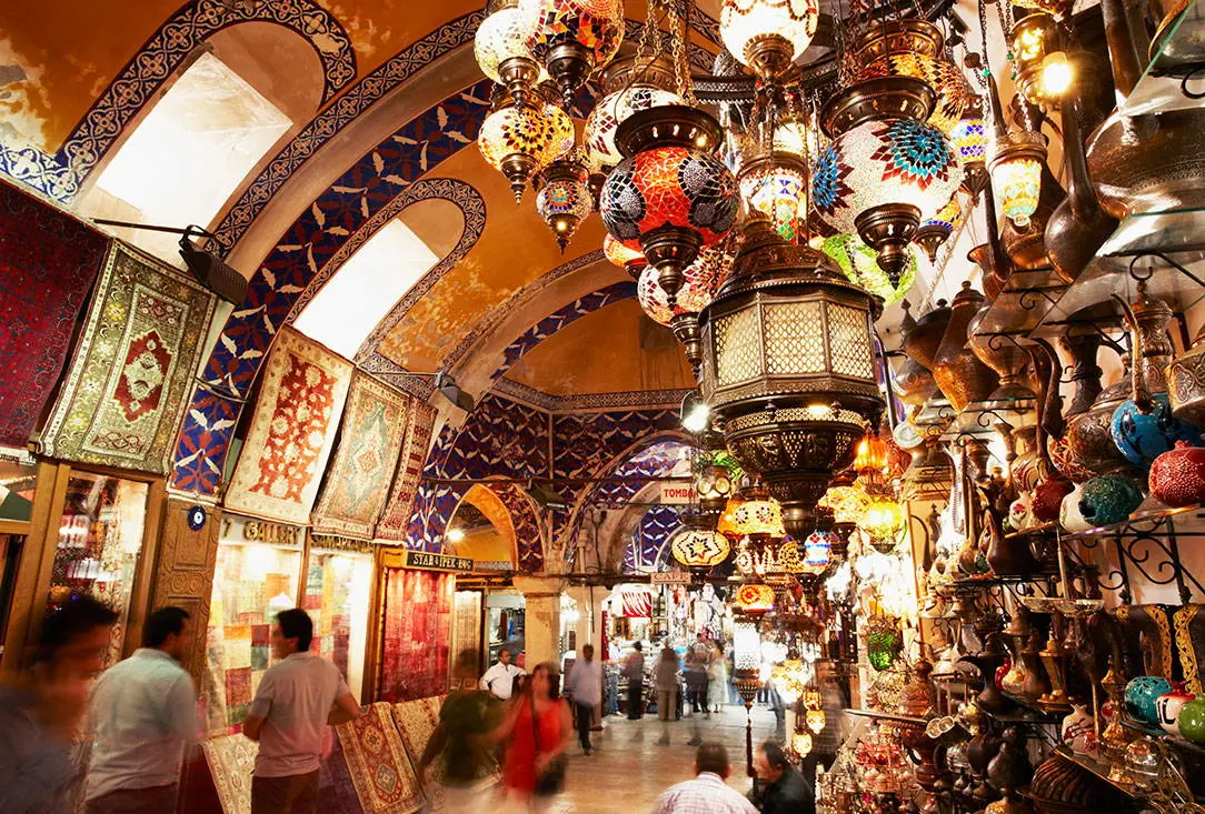 Hanging lamps, rugs and shoppers in a vaulted lane of the Grand Bazaar