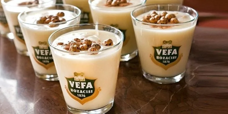 Glasses of Vefa boza topped with cinnamon and roasted chickpeas on a marble counter