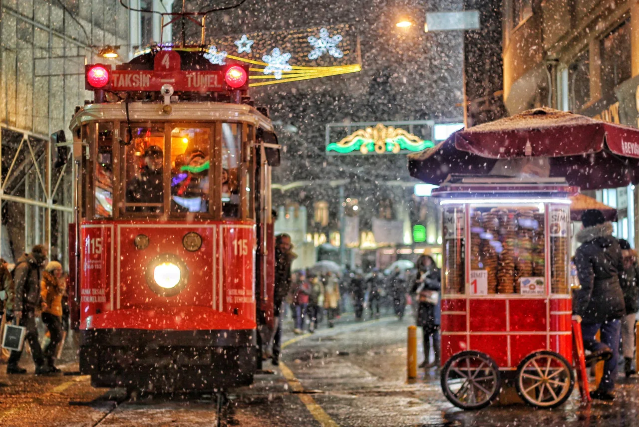 Rote nostalgische Straßenbahn und Simit Cart auf İstiklal Avenue bei Schneefall in der Nacht