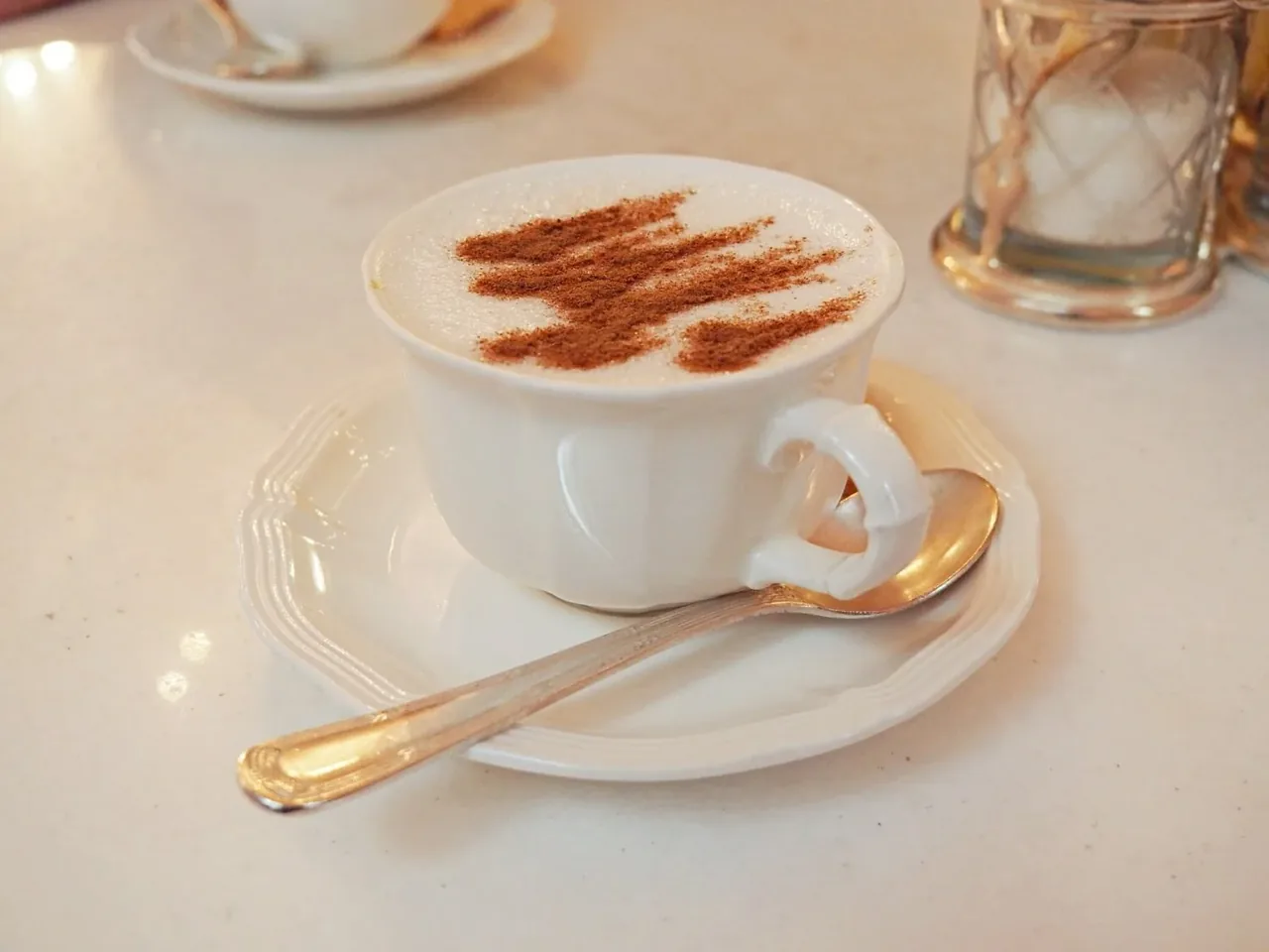 A white cup of salep dusted with cinnamon, with a spoon resting on its saucer